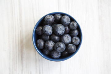 Blueberries in a blue bowl, top view. Fresh bilberry on white wooden table. Healthy eating concept.