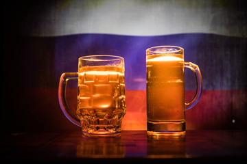 Creative concept. Beer glasses on table at dark toned foggy background with blurred view of flag of Russia. Support your country with beer concept.