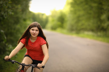 Fototapeta na wymiar teenager girl with long brown hair ride bicycle on country road through the forest close up photo