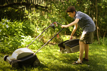 teenager boy mooving lawn in green summer garden