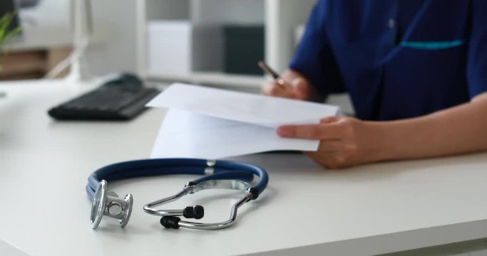 Cropped image of stethoscope on table in focus in foreground, rear doctor filling papers.