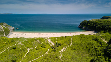 Aerial drone view of a beautiful sandy beach inside a bay surrounded by cliffs and farmland (Barafundle Bay, Wales)