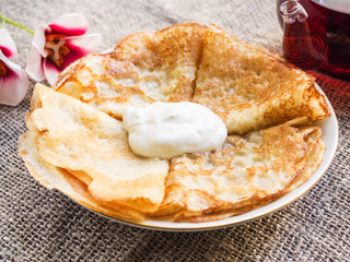 Pancakes on a plate with sour cream and teapot with tea