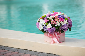 a beautiful bouquet in a box lies on the edge of a pool with blue water