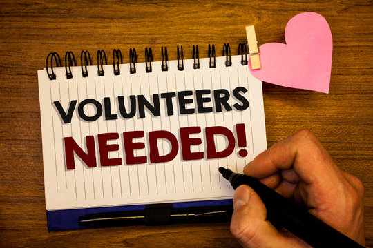 Conceptual hand writing showing Volunteers Needed Motivational Call. Business photo text Social Community Charity Volunteerism Human hand retain black pen notepad with words on paper pink heart.