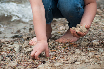 closeup of feet of child playing on the beach with stone