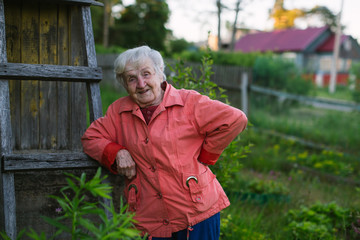 An elderly woman stands near her house in the village.