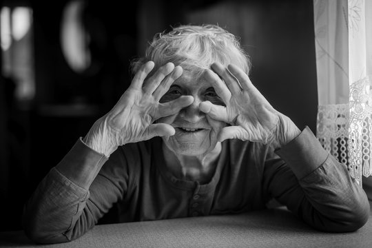 Portrait of an elderly woman covering her face with her hands playfully peeking through her fingers. Black and white photo.