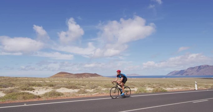 Cycling - Road biking cyclist man training on bike. Professional cycling athlete riding racing bicycle training for competition race on open road. SLOW MOTION RED EPIC.