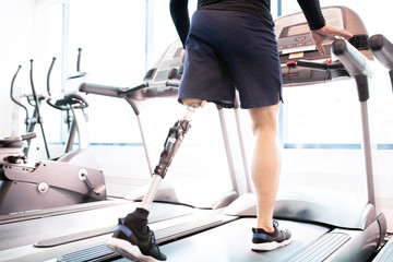 Low angle portrait of unrecognizable muscular man with prosthetic leg using walking on treadmill...