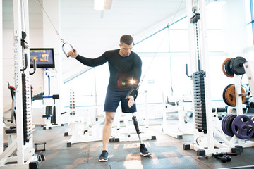 Full length portrait of handsome muscular man with prosthetic leg working out using machines in...