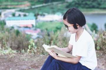 Obraz premium Little kid whit glasses reading a book on mountain