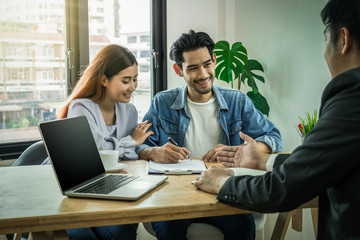 Sale representative present the price and conditon to Asian young couple when signing the contract house purchase or rental on the working space table in new place,Moving and House Hunting concept