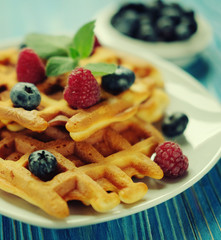 belgian waffles with fresh berrys and sugar powder on white plate, blue wooden background. Flat lay, top view, copy space. Close up.