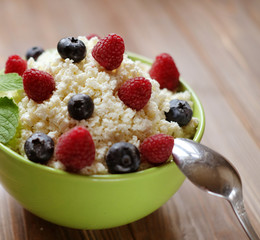 Cottage cheese in green bowl with raspberries and blueberries on wooden background. Healthy Breakfast.