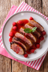 natural food: fried duck breast served with fresh raspberry sauce and mint closeup on a plate. Vertical top view