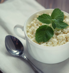 Fresh cottage cheese with mint in a white bowl with spoon on a wooden table. Close up.
