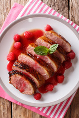 Delicious food sliced grilled duck breast with fresh raspberry sauce and mint closeup on a plate. Vertical top view