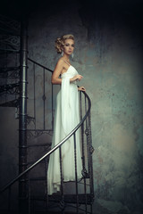 Beautiful young bride in a white dress is standing on a spiral staircase. Wedding concept.
