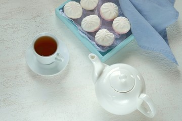 Tea with marshmallows. White teapot,  cup with tea, blue tray with marshmallow on a light background. Tea mood