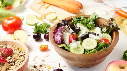 Close up of mixed vegetables salad, muesli and fresh fruits on white background.