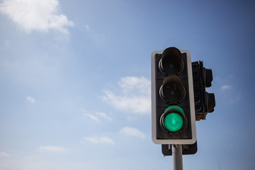 Green traffic light.  Blue sky with few clouds background. Close up under view, copyspace.