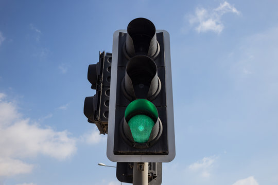 Green traffic light isolated.  Blue sky with few clouds background. Close up under view.