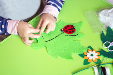 Child making felt soft toy of green leaf and red ladybag . Child DIY activity. Close-up. Children...