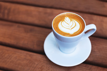 A cup of coffe with latte art on wooden table. Shot at angle with selective focus, italian cappuccino.