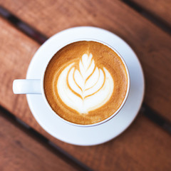 A cup of coffee with latte art on wooden table. Top view, morning mood, italian cappuccino.