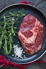 Close-up of raw fresh grass-fed beefsteak with rosemary and sea salt, view from above, vertical shot