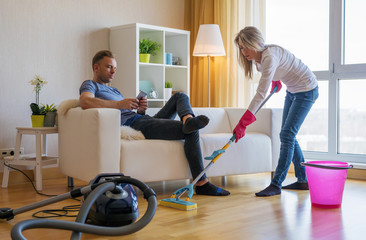 Fototapeta na wymiar Woman cleaning home and man doesn't help her