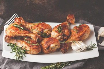 Grilled spicy chicken legs baked with garlic, rosemary and thyme on dark background.