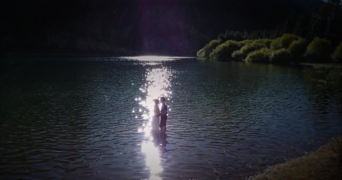 Couple of newlyweds kissing and hugging in the lake after their marriage. Silhoette of the groom and the bride inside the lake at sunset. 4k