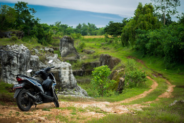 A parked scooter stands on a background of nature with a trail going away and rocks