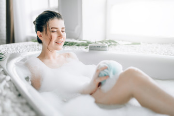 Young woman soaps the body with a sponge