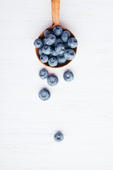 Ripe bluberries in wooden spoon on white wooden table. Top view.