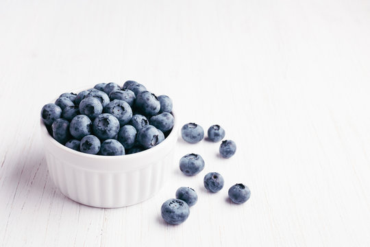 Ripe bluberries in bowl on white wooden table. Shot at angle.