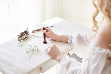 Girl writes a letter to her beloved man, sitting at home at table in a white light dress, purity...
