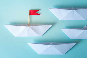 Fototapeta na wymiar Leadership concept using paper ship with red flag on blue background