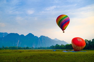 Naklejka premium Colorful hot air balloon float up in the sky at the morning over green fields with mountain background