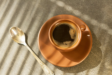 Cup of freshly brewed morning coffee, next to teaspoon, on table
