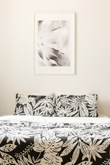 Black and white poster above bed with patterned cushions in minimal bedroom interior. Real photo
