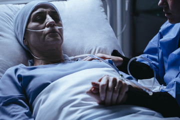 Close-up of passing away senior woman with headscarf after chemotherapy and caregiver