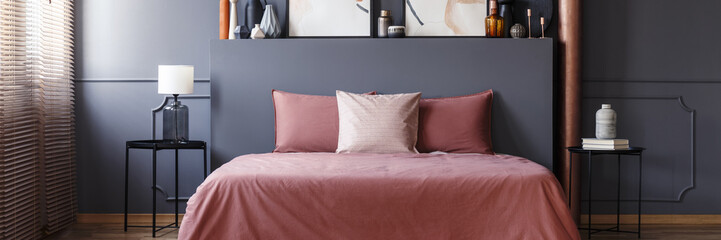 Dirty pink sheets and pillows on double bed standing in grey bedroom interior with metal bedside tables and molding on the wall