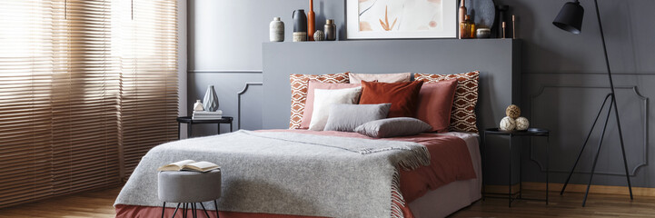 Pouf with open book standing by the king-size bed with pillows in grey bedroom interior with metal...