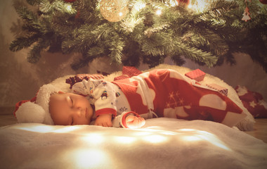 Newborn baby boy sleep under christmas tree wrapped at sleeping christmas bag