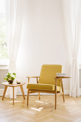 Yellow wooden armchair next to table in white living room interior with drapes. Real photo