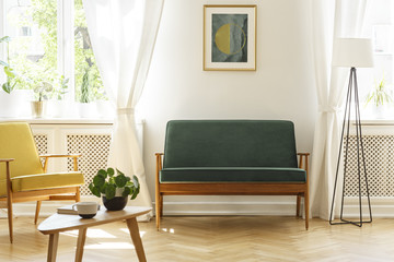 Poster above green bench between lamp and yellow armchair in vintage living room interior. Real...