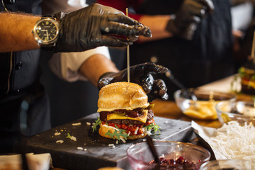Process of cooking burgers. Cropeed view of chef hands in black gloves with prepared cheeseburger,...